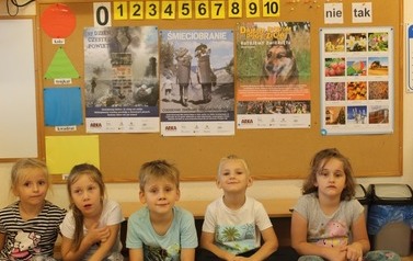 Grupa dzieci w przedszkolu siedząca pod ścianą
