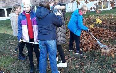 Zdjęcie przedstawia młodzież zagrabiającą liście 