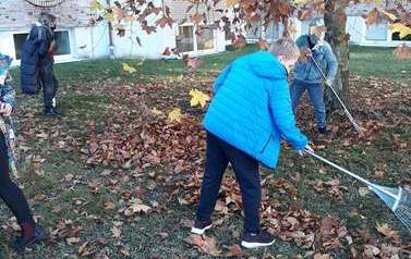 Zdjęcie przedstawia młodzież zagrabiającą liście 